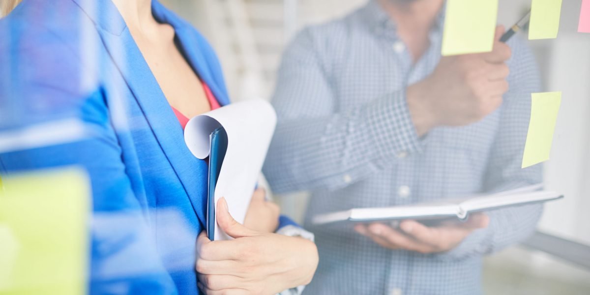 Businesswoman with clipboard listening to colleague idea during discussion of reminders